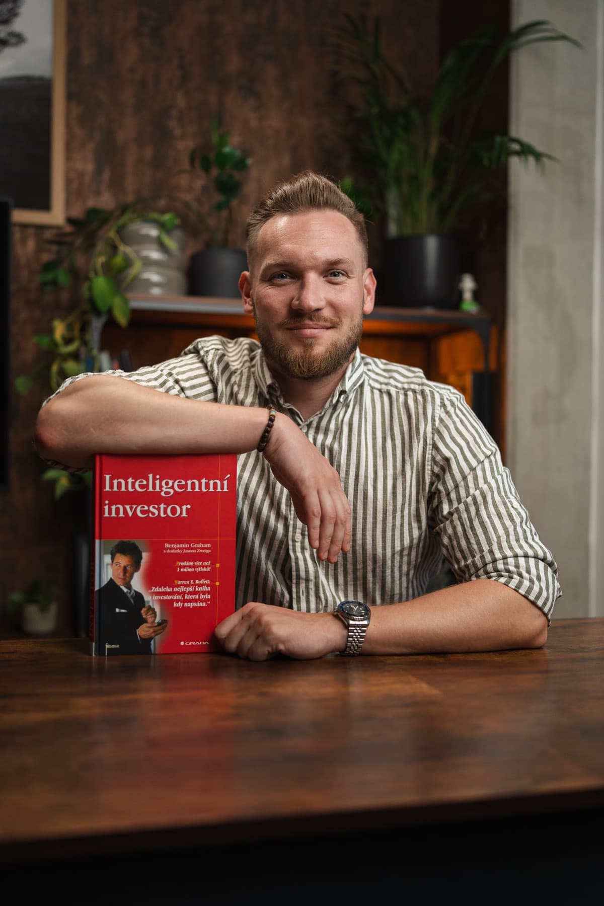 Jakub Kratochvíla opřený o stůl s knihou Inteligentní investor.